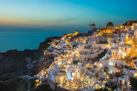 Hvide huse og vindmøller på klippekanten i Oia på Santorini, oplyst i aftenskumringen over havet