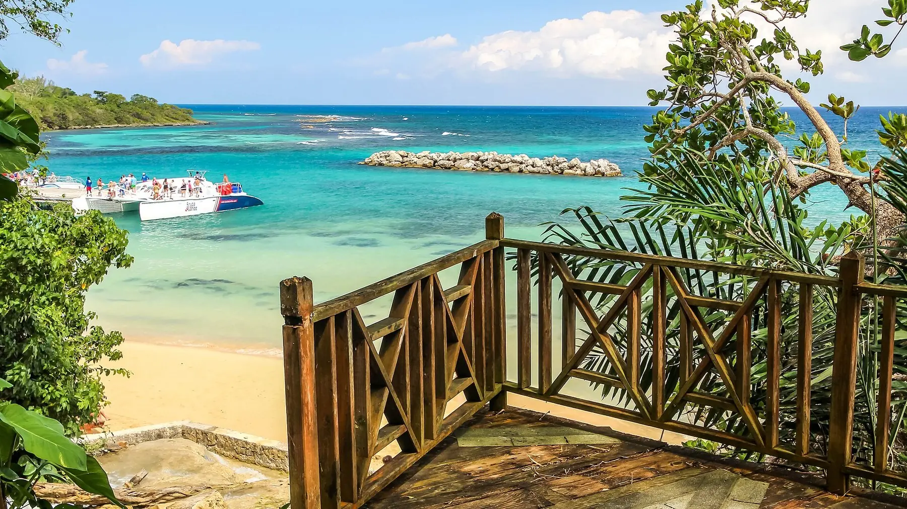 Udsigtsdæk af træ over stranden ved Dunn's River Falls med turkist hav og både