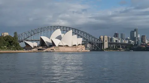 Operahuset i Sydney foran Harbour Bridge og højhusene i centrum set fra vandet i havnen