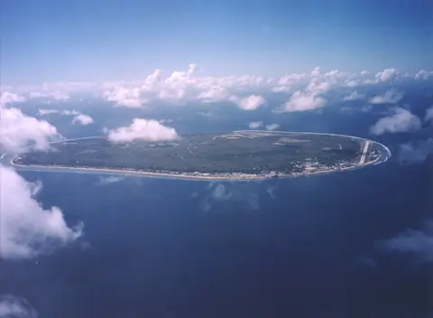 Den runde ø Nauru omgivet af et smalt rev i det blå hav, set fra et fly over skyerne