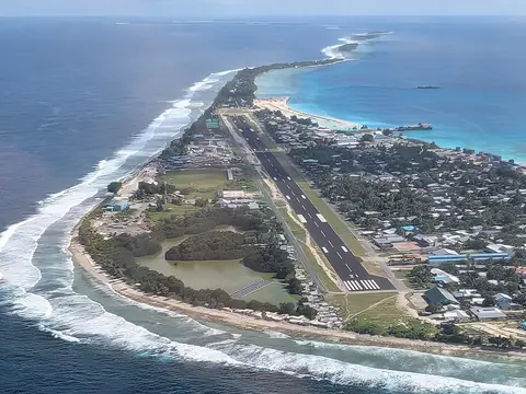 Den smalle atolø Fongafale i Funafuti med landingsbane og huse mellem turkis lagune og hvide brændinger, set fra luften