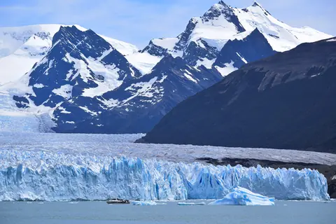 Perito Moreno-gletsjerens blå isfront med en lille turbåd foran og sneklædte bjerge bag i Patagonien